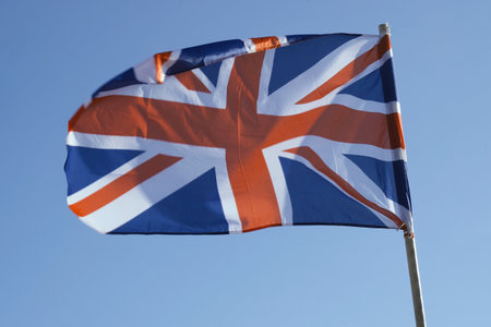 The flag of the United Kingdom of Great Britain, also known as the Union Jack, flying in the wind against a clear blue sky.の写真素材