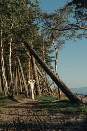 A woman is walking down a dirt road surrounded by tall trees on both sides.の写真素材