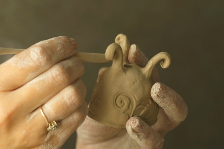 A woman potter decorates a clay product with patterns using a tool. Close-up. Creative hobby.