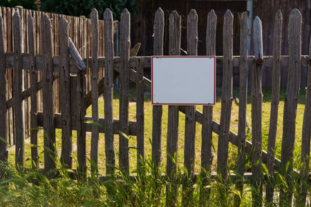 An aged wooden fence stands with a white blank sign affixed, in soft evening light.の写真素材