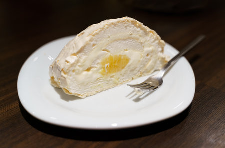A slice of vanilla cake roll with cream filling, served on a plate accompanied by a dessert fork.の写真素材
