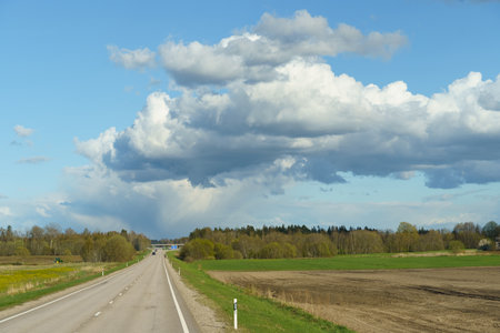 A wide road stretching into the horizon under a sky filled with billowing clouds, creating a dynamic and ever-changing scene.の写真素材