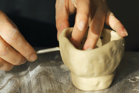 A woman makes holes using a tool in a clay craft - a candlestick. Close-up. Hobbies and creativity.の写真素材