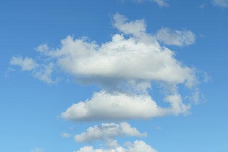 A cluster of puffy clouds peacefully drifts across the clear blue sky on a sunny day.の写真素材