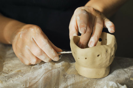 A woman makes holes using a tool in a clay craft - a candlestick. Close-up. Hobbies and creativity.の写真素材