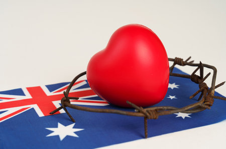 A vibrant red heart wrapped in barbed wire sits atop an Australian flag, depicting a struggle for love and freedom amidst constraints.の写真素材