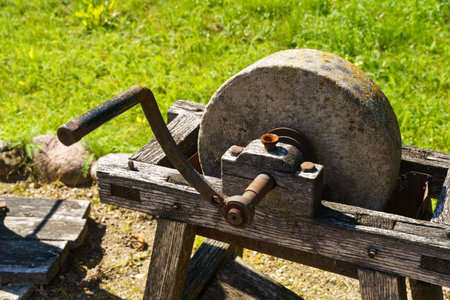 A well-worn grinding wheel sits idle on a rustic wooden stand, with a metal hammer resting atop,...