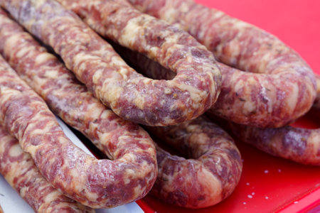 Several raw sausages are piled on a bright red surface, highlighting their marbled texture. The...