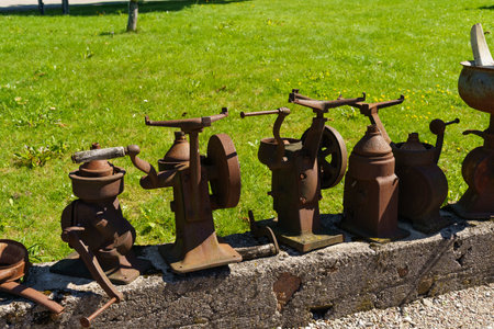 A collection of old, rusty metal equipment and tools, likely from a bygone era, showcased outside on a bright, grassy backdrop.の写真素材