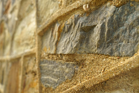 Detailed close-up view of a stone wall with sand grains layered on its surface, highlighting the texture and abstraction of the elements.の写真素材