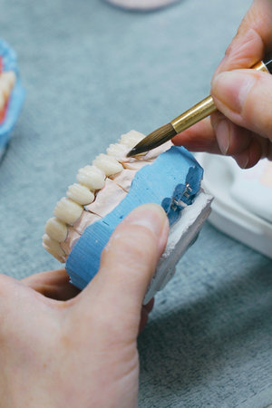 A close-up of a dental technician holding a toothbrush in their right hand, part of the process of...