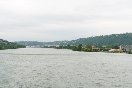 A wide shot of the Isere River flowing through the city of Grenoble, France, with a view of the surrounding mountains in the background on a cloudy day.の写真素材