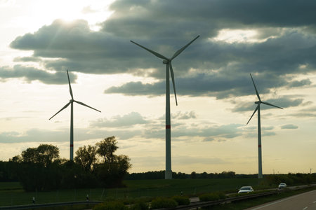 A car travels down a road lined with towering wind turbines. The vehicle moves alongside the...