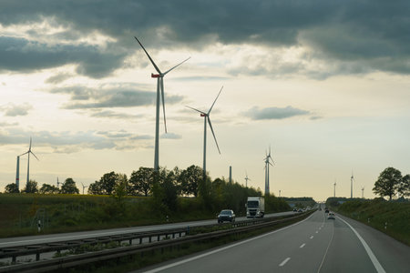 A truck drives down a highway next to a row of wind turbines under a clear sky.