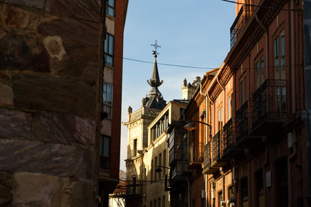 Sunlight bathes the stone facades of a historic street in Astorga, Spain, revealing intricate details and a glimpse of a charming church tower in the distance.の写真素材