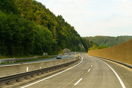 A serene highway weaves through verdant hills, as cars traverse the smooth asphalt under a gentle sunset glow, creating a picturesque evening journey through nature.の写真素材