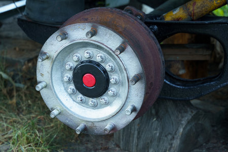 A weathered wheel hub rests on the ground, showing its worn metal surface and unique design. Nature intertwines with the vehicle remnants, creating a blend of industrial history and natural decay.の写真素材