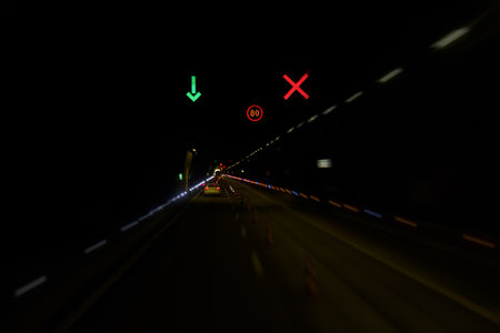 A tunnel at night is filled with streaks of light from moving vehicles. Traffic signals guide drivers, showcasing a vibrant display of red and green lights.の写真素材