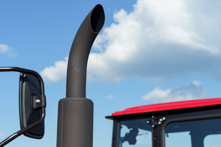 A close-up view of a tractor's exhausted pipe stands proudly against a backdrop of blue sky and white clouds. The setting highlights the power of agricultural machinery in action.の写真素材