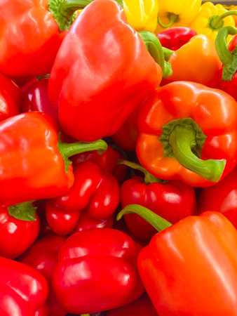 A colorful assortment of fresh red and yellow bell peppers fills the market stall, showing their glossy textures and rich colors. Each pepper gleams under the soft light, inviting shoppers.の写真素材