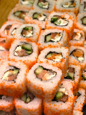 Stacks of vibrant sushi rolls feature layers of fresh fish, crisp cucumber, and creamy filling, all wrapped in bright orange tobiko. A delightful culinary display perfect for sharing.の写真素材