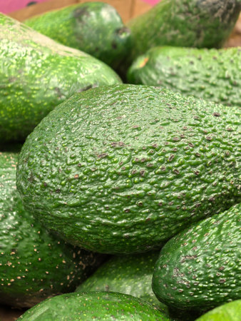 A lush display of avocados rests in a bustling marketplace, showing their rich green hues and textured skin. The lively atmosphere invites shoppers to explore fresh produce.の写真素材