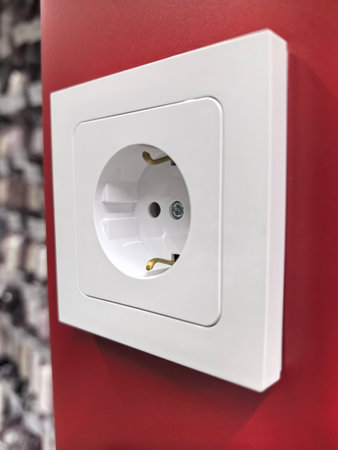 A white electrical outlet is mounted on a bright red wall, surrounded by a textured, black and white...