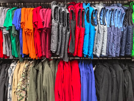 Hanging racks showcase an array of colorful apparel in a busy retail space. Shoppers browse various styles and hues, creating a lively atmosphere in the store.