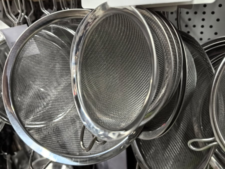 Various metal strainers hang neatly, showcasing their fine mesh and polished surfaces. They await passionate cooks eager to elevate their culinary experiences in the kitchen.の写真素材
