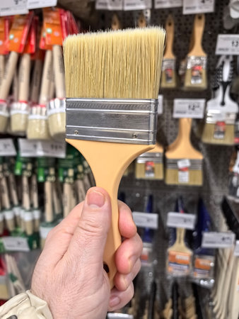 A hand holds a paintbrush in a store, surrounded by various painting tools. Shelves are lined with different brushes, highlighting options for upcoming renovation tasks.の写真素材