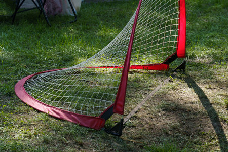 A vibrant red goal net stands on a grassy patch under the warm sun, inviting playful activities and friendly matches. Shadows stretch across the ground, hinting at the fun ahead.の写真素材