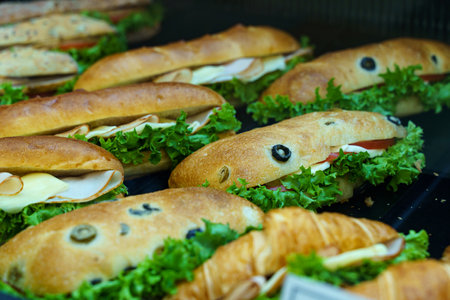 Freshly made sandwiches filled with leafy greens, tomatoes, and various meats are presented on a platter, showcasing vibrant colors and inviting textures perfect for any gathering.の写真素材