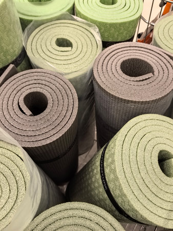 A variety of green and gray yoga mats are neatly rolled and stacked inside a shopping cart, showing their soft textures and patterns, perfect for practicing mindfulness.の写真素材
