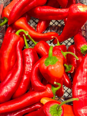 Bright red peppers of various shapes fill a market basket, showing their glossy skin under natural light. Each pepper adds to the rich, colorful display of fresh produce.の写真素材