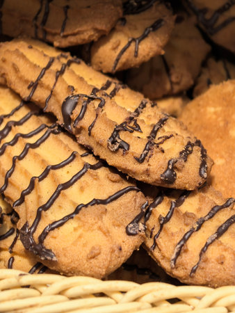 A tempting assortment of cookies lies in a woven basket, showcasing their golden-brown crusts and rich chocolate drizzles. The inviting aroma fills the air, making it hard to resist.の写真素材