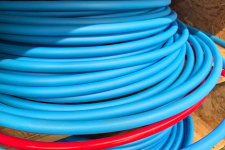 On a bright day, blue and red tubing coils rest playfully against each other in a workspace. The structured arrangement creates a striking contrast of colors and texture.の写真素材