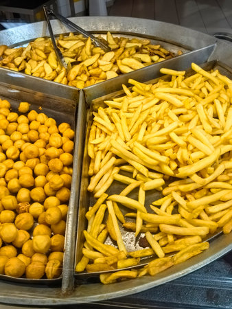 Freshly prepared golden snacks fill a large tray at a lively street market in the evening. The aroma of the fried delicacies draws in hungry customers eager to taste the crispy delights.の写真素材
