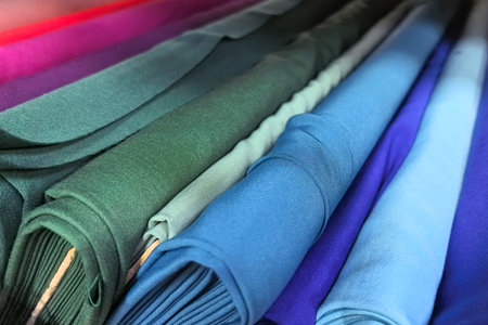 Colors blend seamlessly as rolls of fabric are neatly arranged, showing a spectrum of blues and greens. Tailors and designers can find inspiration in this fabric collection for countless projects.の写真素材