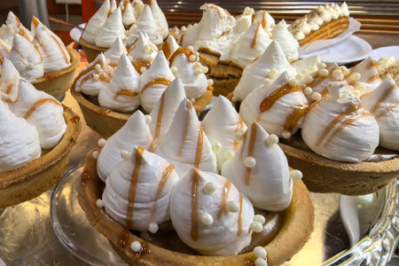 Meringue tarts with fluffy peaks are beautifully displayed, drizzled with caramel and adorned with sweet pearls. The dessert radiates a tempting allure, perfect for any celebration or gathering.の写真素材