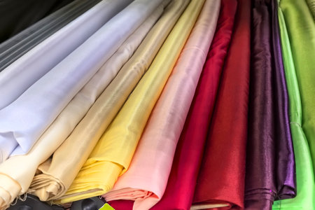 Brightly colored rolls of fabric are neatly arranged in a textile shop, showcasing an array of hues from rich reds to soft pastels. The display invites creativity and inspiration.の写真素材