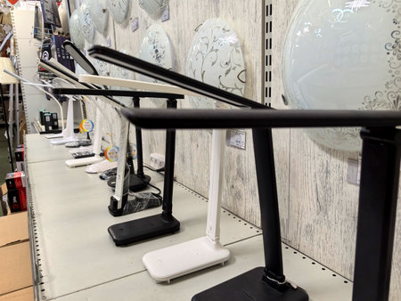 A row of stylish desk lamps in contrasting colors showcases contemporary design. These lamps are neatly arranged on a display table, inviting potential buyers to explore options.の写真素材