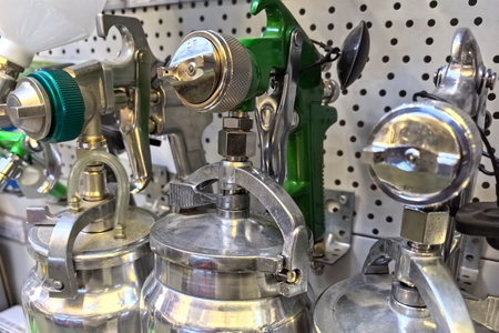 Various pneumatic paint sprayers are neatly organized on a pegboard in a workshop. The tools shimmer with metal finishes and are ready for paint application, showing efficiency and precision.の写真素材