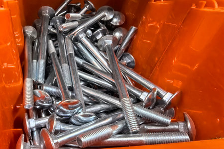Various sizes of shiny metal bolts and screws are neatly organized in a large bright orange container. The setting suggests a bustling hardware store focused on DIY projects.の写真素材