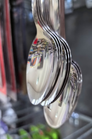 Spoons gleam in bright light as they hang in an organized row, showcasing their sleek design. The reflections capture the vibrant atmosphere of a bustling kitchenware store.の写真素材