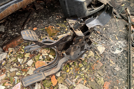Rusting car components rest on shattered concrete and debris, hinting at a once-bustling repair shop. Nature reclaims this site under overcast skies, capturing a moment of decay.の写真素材