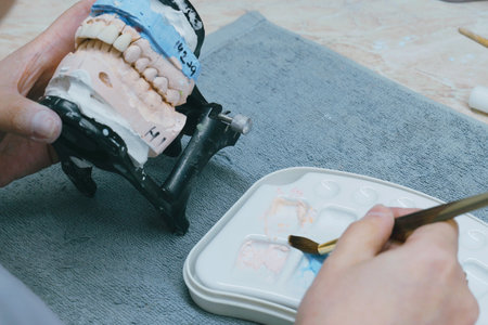 Skilled dental technician meticulously crafts ceramic dentures using precision tools. The workspace is organized, showcasing vibrant materials and detailed techniques in progress.の写真素材