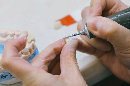 A skilled dental technician carefully grinds a denture piece with precision tools, ensuring a...