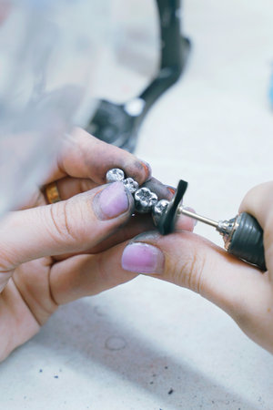 A skilled dental technician meticulously grinds and molds metal dentures in a workshop setting. Using specialized tools, they enhance each detail to ensure a perfect fit for patients.の写真素材