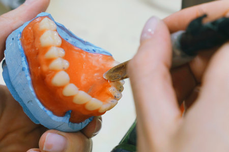 A skilled dental technician meticulously shapes wax into detailed dentures. The workspace is filled...