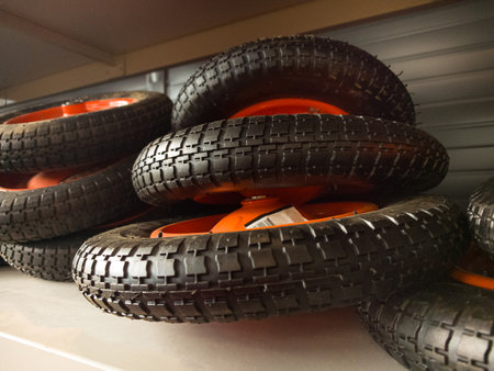 A variety of black rubber wheels with vibrant orange rims are carefully arranged on a workshop...